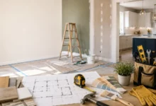 Modern home renovation workspace with architectural blueprints, paint samples, flooring materials, tools, and a partially remodeled kitchen, illustrating a complete home improvement project.